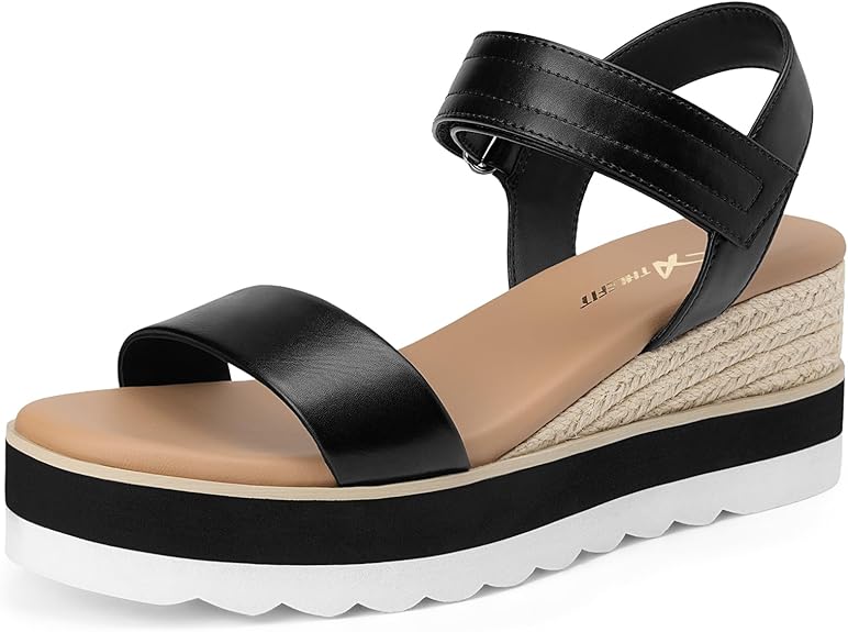 A black strappy platform sandal with an ankle strap and buckle closure, tan cushioned footbed, espadrille-style trim, and a thick white wavy sole.