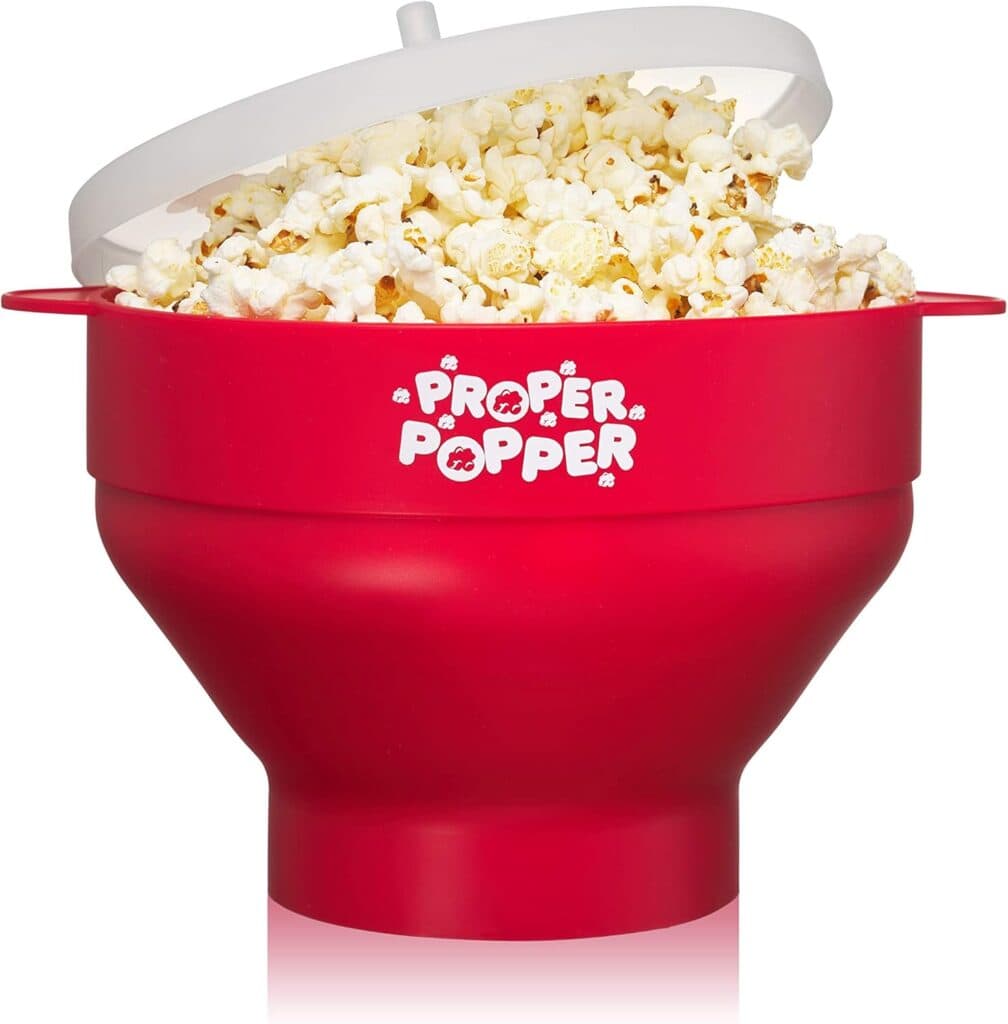 A red silicone popcorn maker labeled "Proper Popper," filled with popcorn and topped with a translucent white lid, is shown on a white background.
