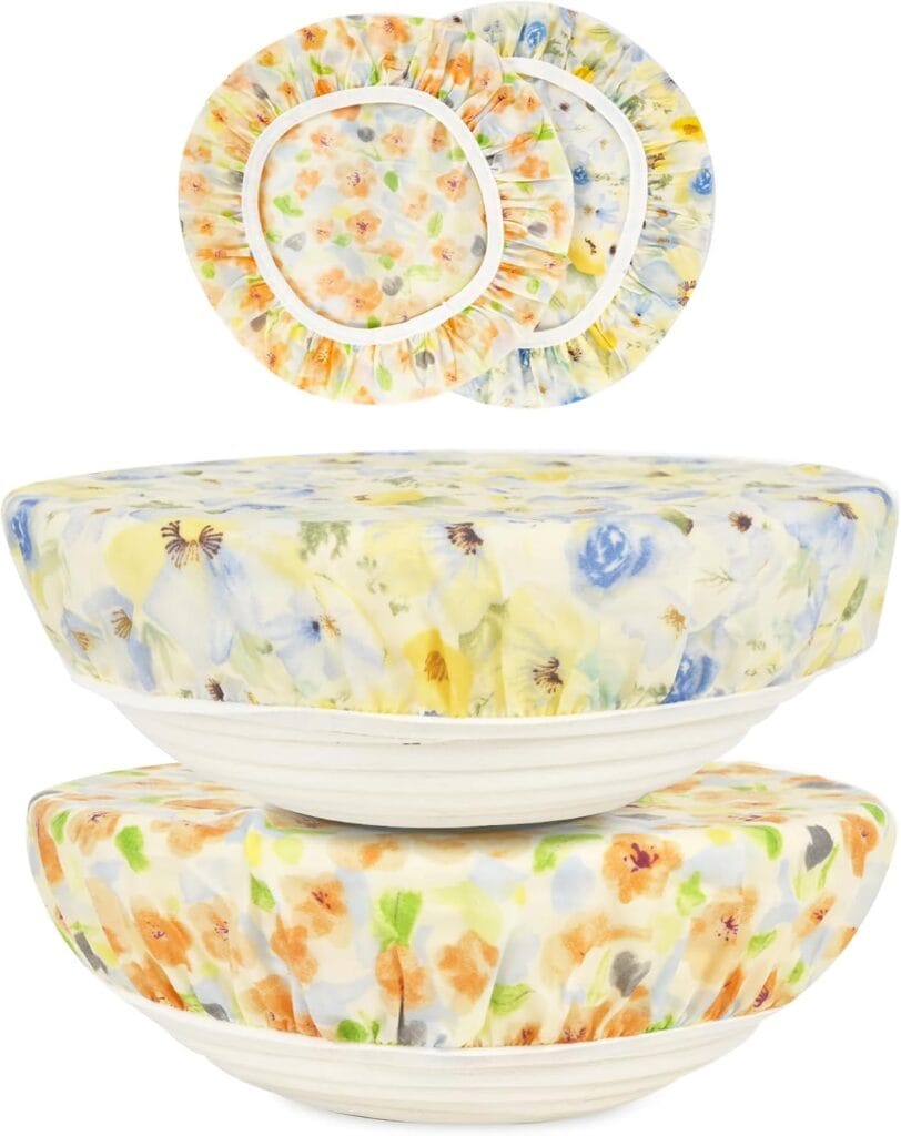 Three ceramic bowls covered with reusable fabric bowl covers featuring a pastel floral pattern, with the bowls stacked and three additional covers laid flat above them.