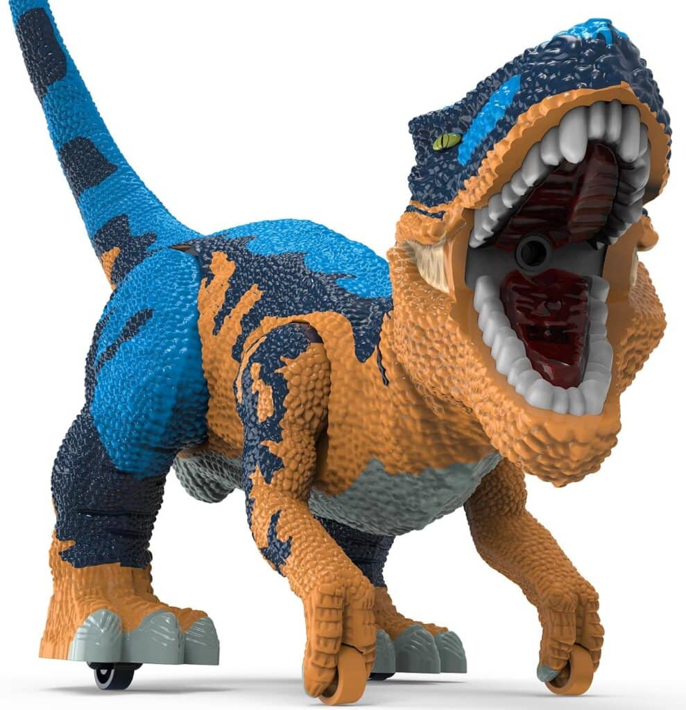 A toy dinosaur with blue, orange, and black textured skin, a large open mouth showing sharp teeth, green eyes, and wheels on its feet, positioned as if roaring or moving forward.