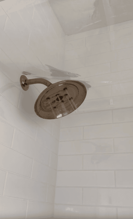 A bronze showerhead sprays water in a tiled shower retreat with white subway tiles on the walls.
