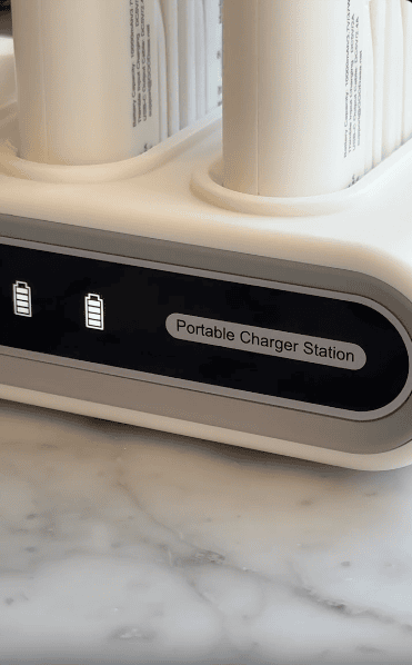 A close-up of a white portable charger station with two battery icons and a label that reads "Portable Charger Station," placed on a marble surface.