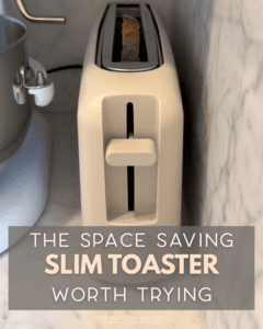 A slim, cream-colored toaster with a single slot sits on a marble countertop beside a stand mixer and a mini waffle maker. Text overlay reads: "The space saving slim toaster worth trying.