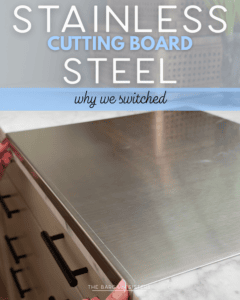 A person places a stainless steel cutting board on a white kitchen counter, with black-handled drawers below. Text over the image reads, "Stainless Steel Cutting Board - why we switched.