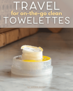 A small round container of pocket sized travel towelettes sits open on a marble surface, with a towelette partially pulled out. Text above reads, "Travel for on-the-go clean towelettes.