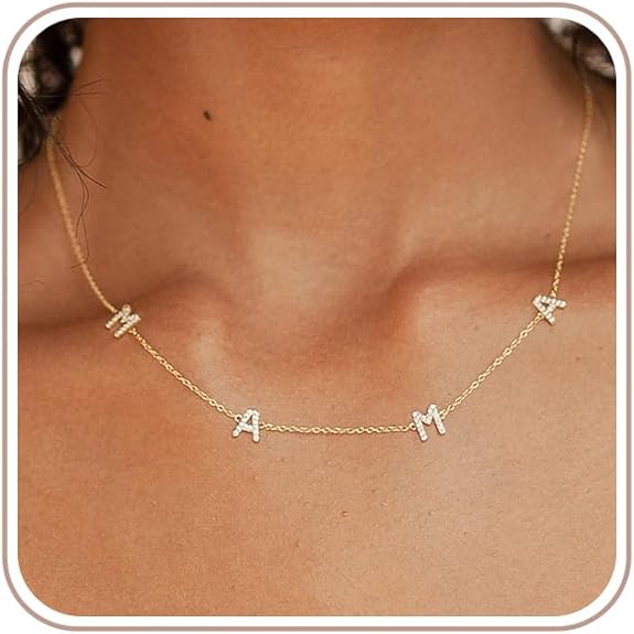 A close-up of a woman’s neck wearing a delicate gold chain necklace with four letter charms spelling “MAMA,” each letter adorned with small sparkling stones.
