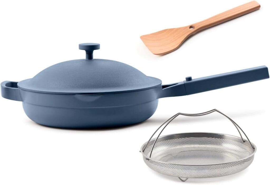 A blue nonstick skillet with a matching lid, long handle, wooden spatula, and round metal mesh steamer basket are arranged on a white background—perfect for upgrading your kitchen during Thursday Deals.