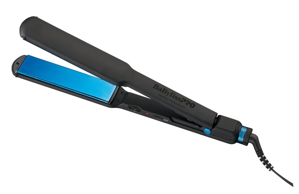 A black and blue BaBylissPRO Nano Titanium hair straightener with a wide flat iron plate and a hinged handle, shown plugged in with the cord extending from the base.