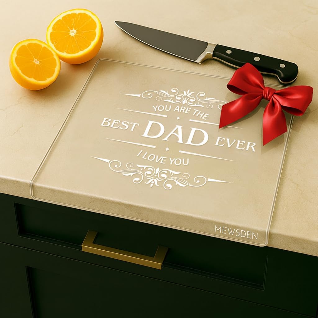 A glass cutting board with the inscription "You are the best Dad ever, I love you" and a red bow sits on a dark kitchen counter beside a knife and two orange halves.