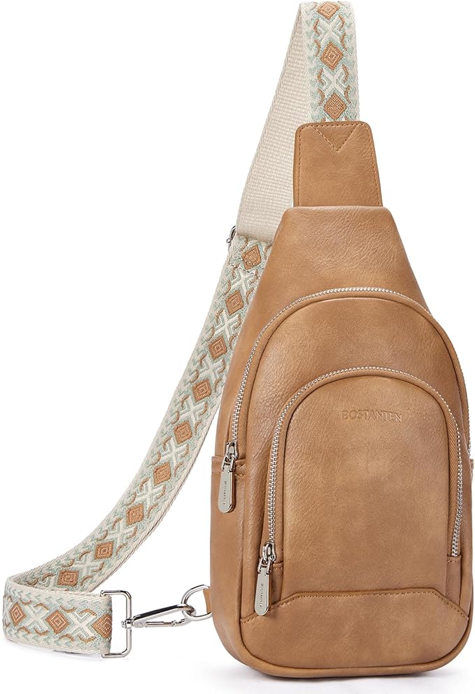 A tan leather crossbody sling bag with two zippered compartments and a wide adjustable strap featuring a geometric pattern in cream and tan.