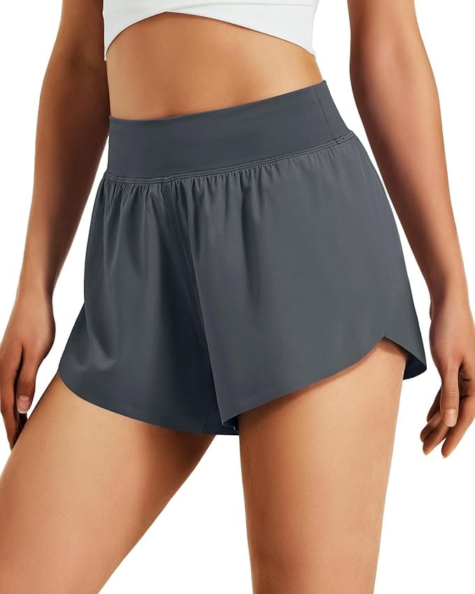 A person wearing a white sports top and high-waisted, dark gray athletic shorts with a curved hem, posing against a white background.
