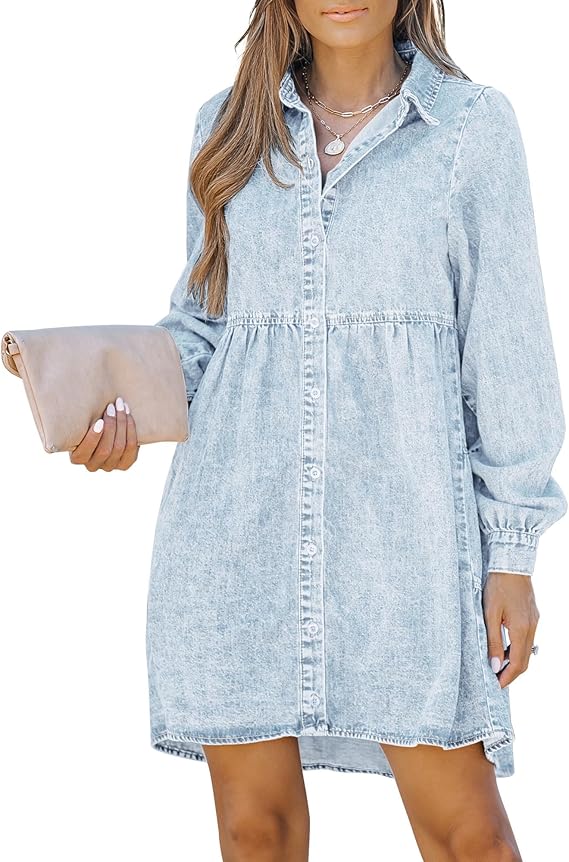 A woman wears a light blue, button-down denim shirt dress with long sleeves. She holds a beige clutch and accessorizes with layered necklaces. Her hair is styled in loose waves.