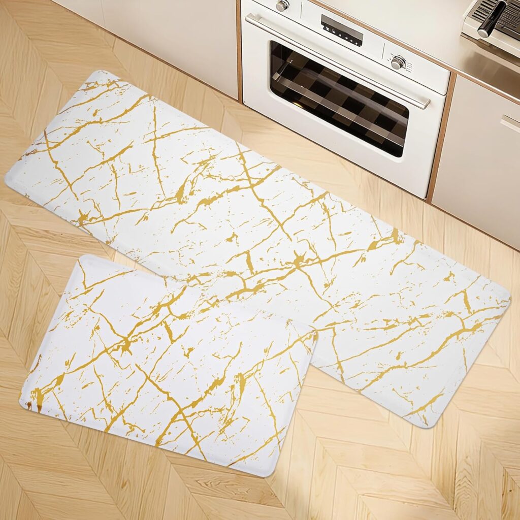 Two rectangular kitchen rugs with a white background and gold marble-like streaks are placed on a light wood herringbone floor in front of an oven and cabinets—perfect for updating your space with our exclusive Wednesday Deals.