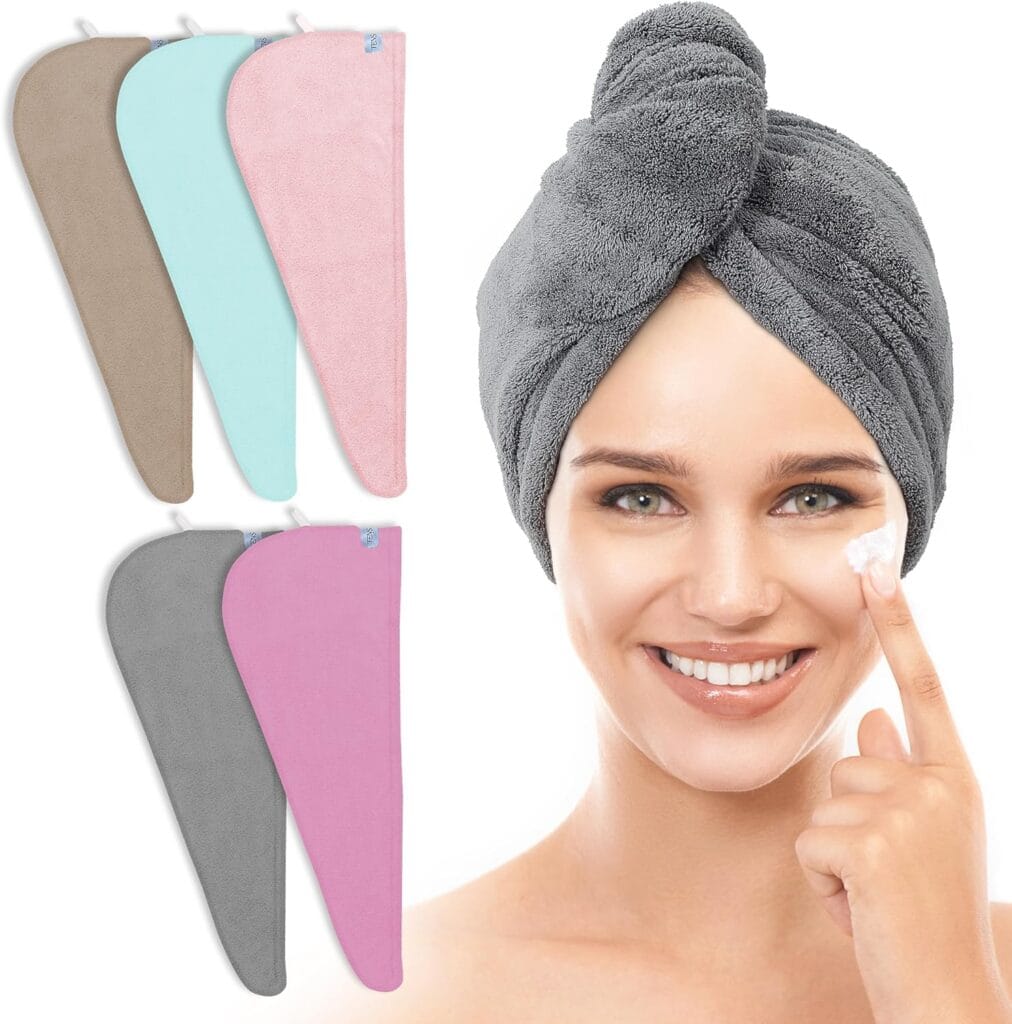 A smiling woman with a gray microfiber hair towel wrapped on her head applies cream to her cheek. Beside her are four microfiber hair towels in beige, light blue, pink, and gray, shown flat.