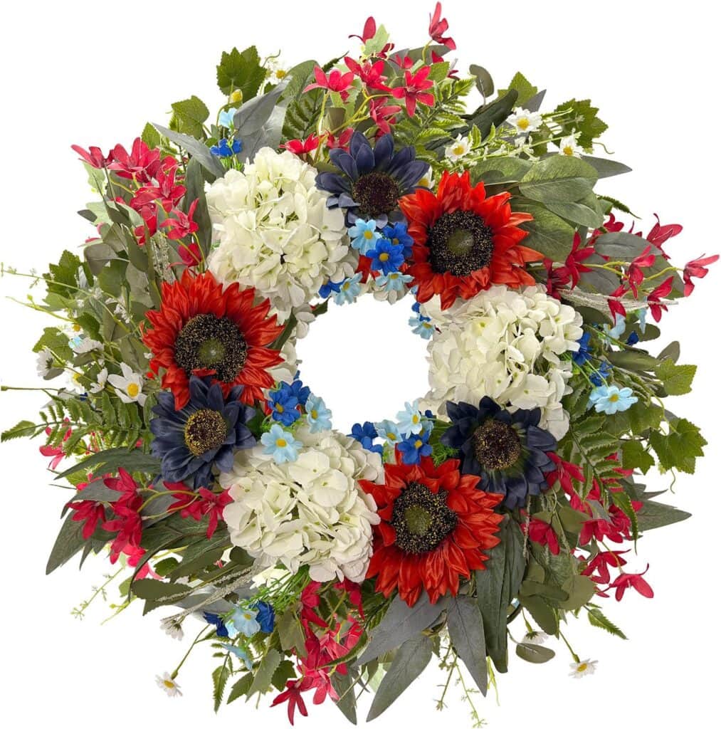A decorative wreath featuring red, white, and blue flowers—sunflowers, hydrangeas, and small blue blossoms—surrounded by green leaves and foliage. Perfect for your home décor and available now with exclusive Friday Deals!.