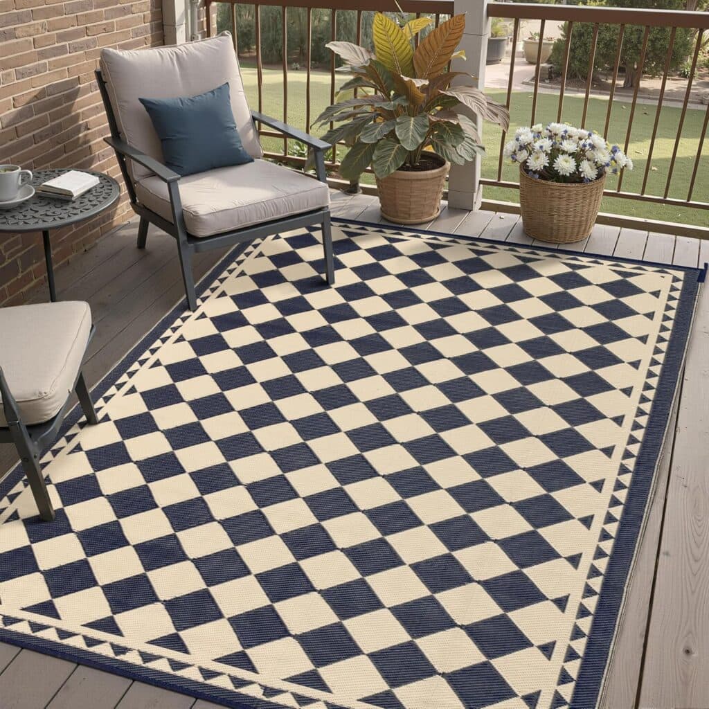 A checkered blue and white rug on a porch with cushioned chairs, a small table with a cup and saucer, and potted plants near the railing—perfect for relaxing, especially when styled with favorites from our Friday Deals.