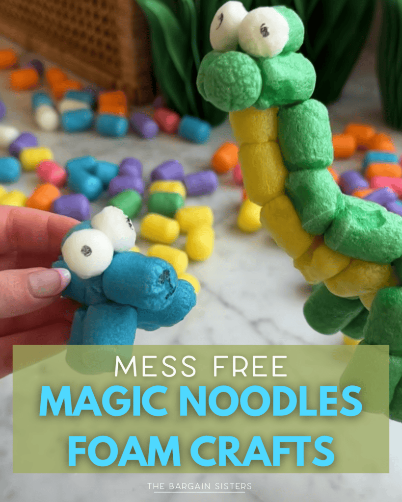 A hand holds a blue Magic Noodles creature with googly eyes next to a larger green and yellow foam dinosaur. Colorful foam noodles are scattered on a table in the background. Text overlay reads: "Mess Free Magic Noodles Foam Crafts for Kids.