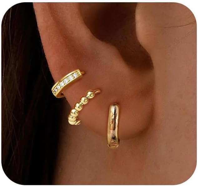Close-up of an ear wearing three gold ear cuffs: one with small clear stones, one with round gold beads, and one smooth and plain.