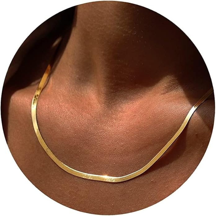 A close-up of a person's neck wearing a flat, shiny gold chain necklace against a brown skin tone, set within a circular frame.