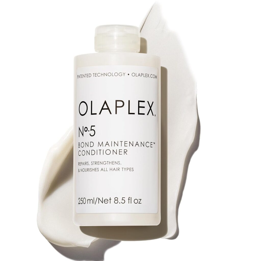 A white bottle of Olaplex No. 5 Bond Maintenance Conditioner sits on a creamy, textured surface. The label states it repairs, strengthens, and nourishes all hair types; the bottle is 250 ml (8.5 fl oz).