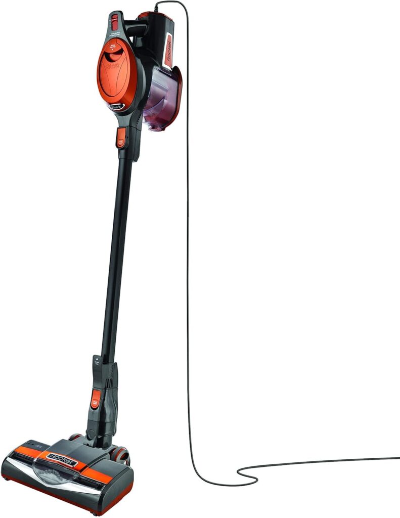 A corded upright vacuum cleaner with a red and black design, featuring a transparent dust container and a long power cord extending to the right.