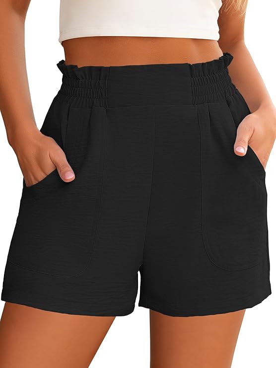 A person wearing high-waisted black shorts with an elastic waistband and pockets, standing with hands in the pockets. The top part of a white crop top is also visible.