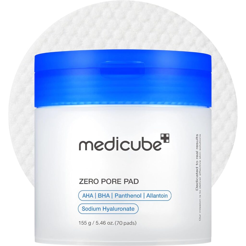 A white jar with a blue lid labeled "medicube ZERO PORE PAD," featuring ingredients such as AHA, BHA, Panthenol, Allantoin, and Sodium Hyaluronate. The background shows a textured, round cotton pad.