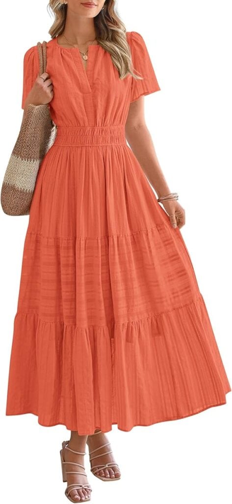 Woman wearing a short-sleeve, ankle-length, tiered orange dress with a cinched waist, holding a woven tote bag, accessorized with bracelets, necklace, and sandals.