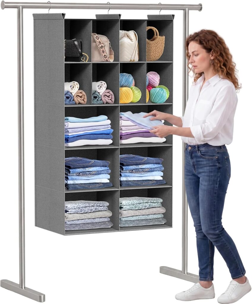 A woman stands next to a gray hanging organizer filled with neatly folded clothes, towels, yarn, and bags on a metal rack. She is folding laundry in a white shirt and blue jeans, making the most of Tuesday Deals for organized living.