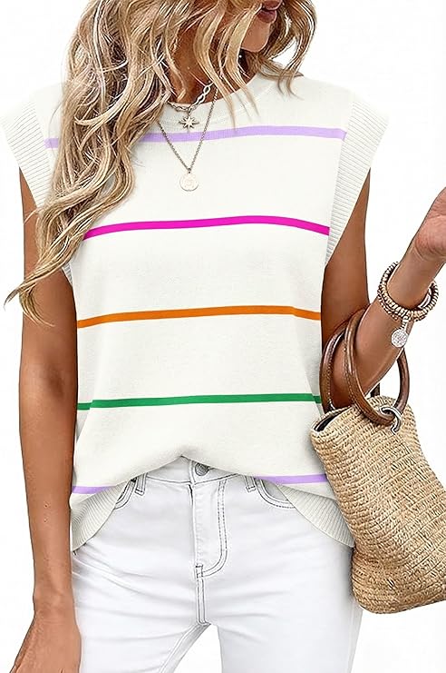 A woman wearing a sleeveless white knit top with colorful horizontal stripes, white pants, layered necklaces, and bracelets holds a woven straw bag. Her wavy blonde hair stands out against the plain white background—perfect for Tuesday Deals.