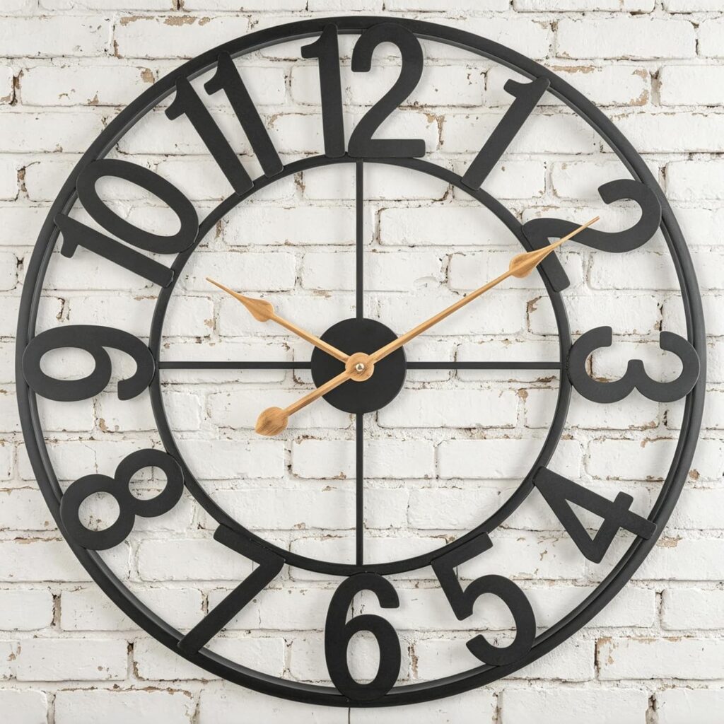 A large black metal wall clock with gold hands hangs on a white painted brick wall. The clock's bold, oversized numbers and open frame design stand out—perfect for catching Tuesday Deals on stylish home décor. Time shown is approximately 10:13.