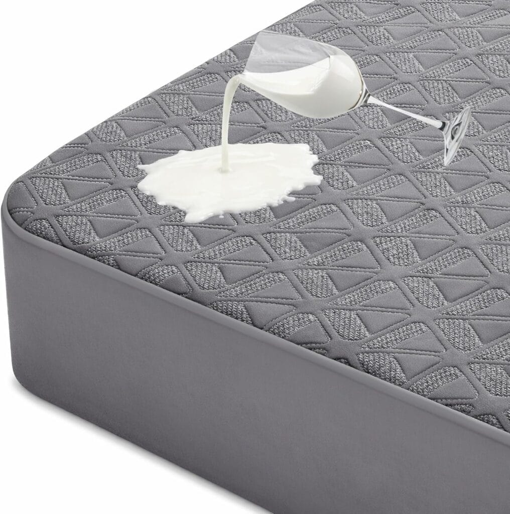 A glass of milk is tipped over, spilling milk onto a gray, textured mattress, demonstrating the mattress’s liquid-resistant surface.