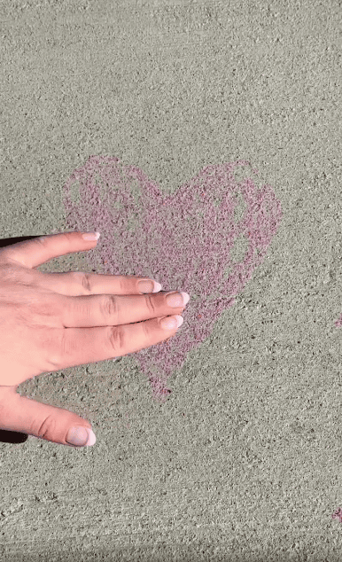 A hand with neatly manicured nails rests on concrete next to a pink heart drawn with chalk.