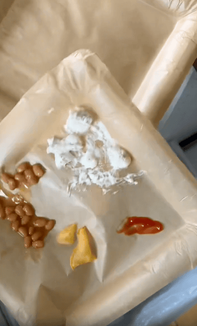 A beige tray with small portions of beans, mashed potatoes, two potato wedges, and a small amount of ketchup, all separated into different sections.