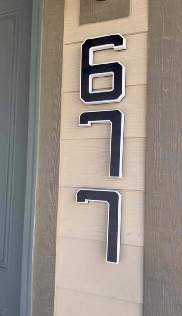 Large black house numbers "617" with white trim are mounted vertically on beige horizontal siding next to a blue door.