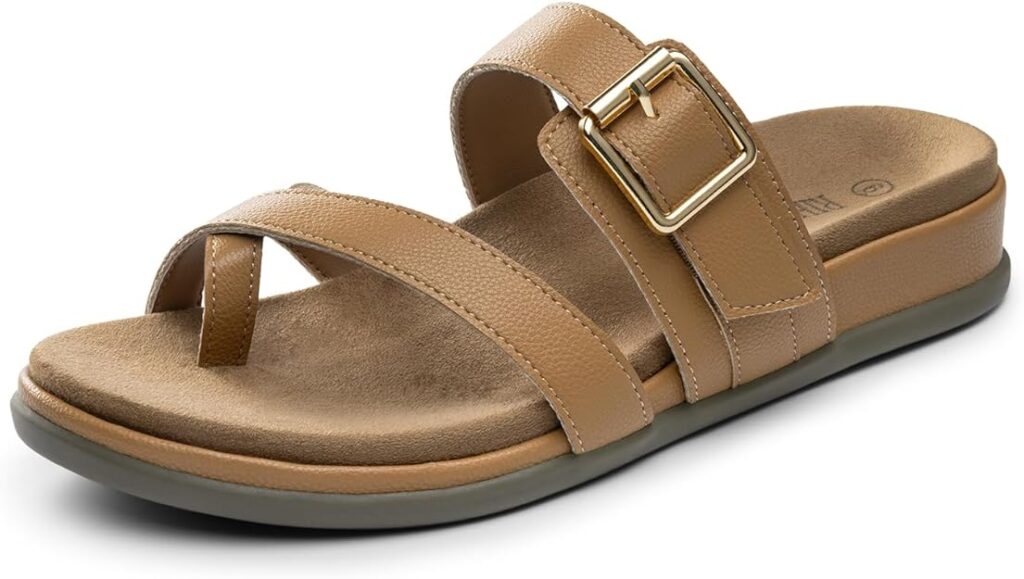 A tan, open-toe sandal with a cushioned sole, a wide strap featuring a gold buckle, and an additional strap crossing over the toe area. The sandal has a low, flat heel.