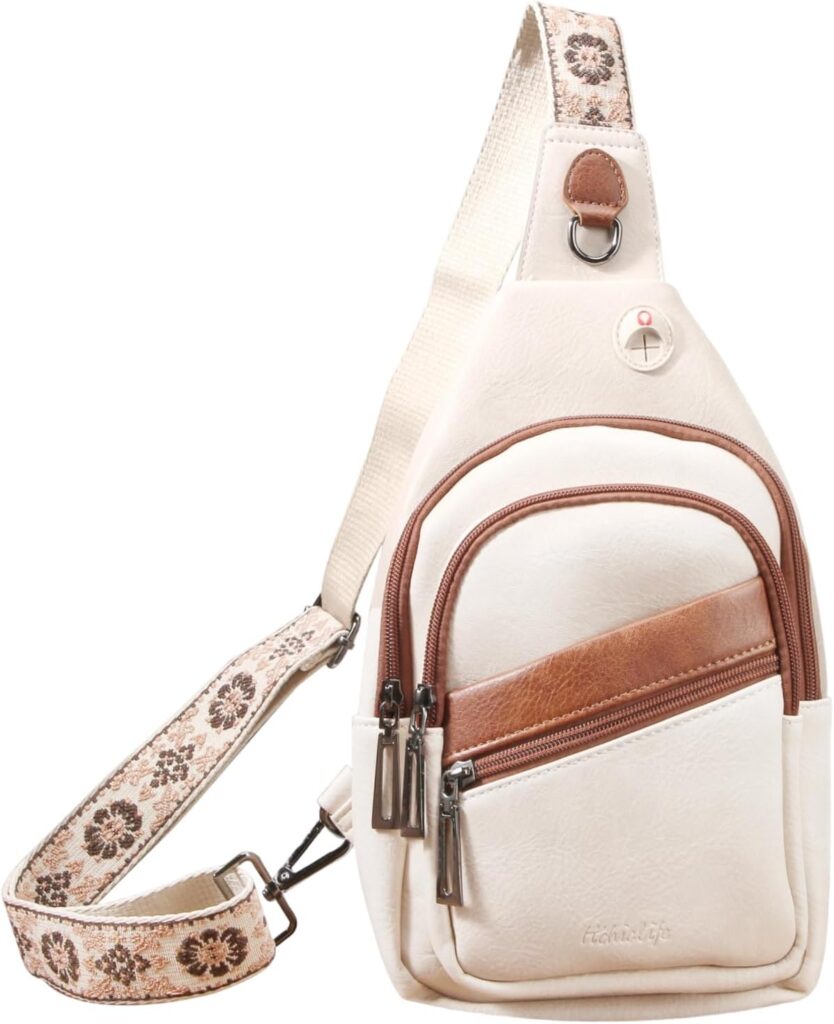 A cream-colored crossbody sling bag with brown accents, two front zipper pockets, and an adjustable strap featuring a floral pattern. The bag has a minimalist design and a small leather patch near the top.
