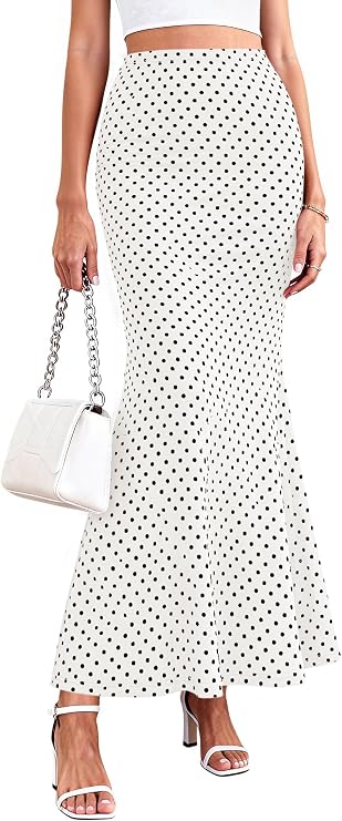 A woman wearing a white high-waisted, ankle-length skirt with black polka dots, a white crop top, white heeled sandals, and holding a white handbag with a chain strap.