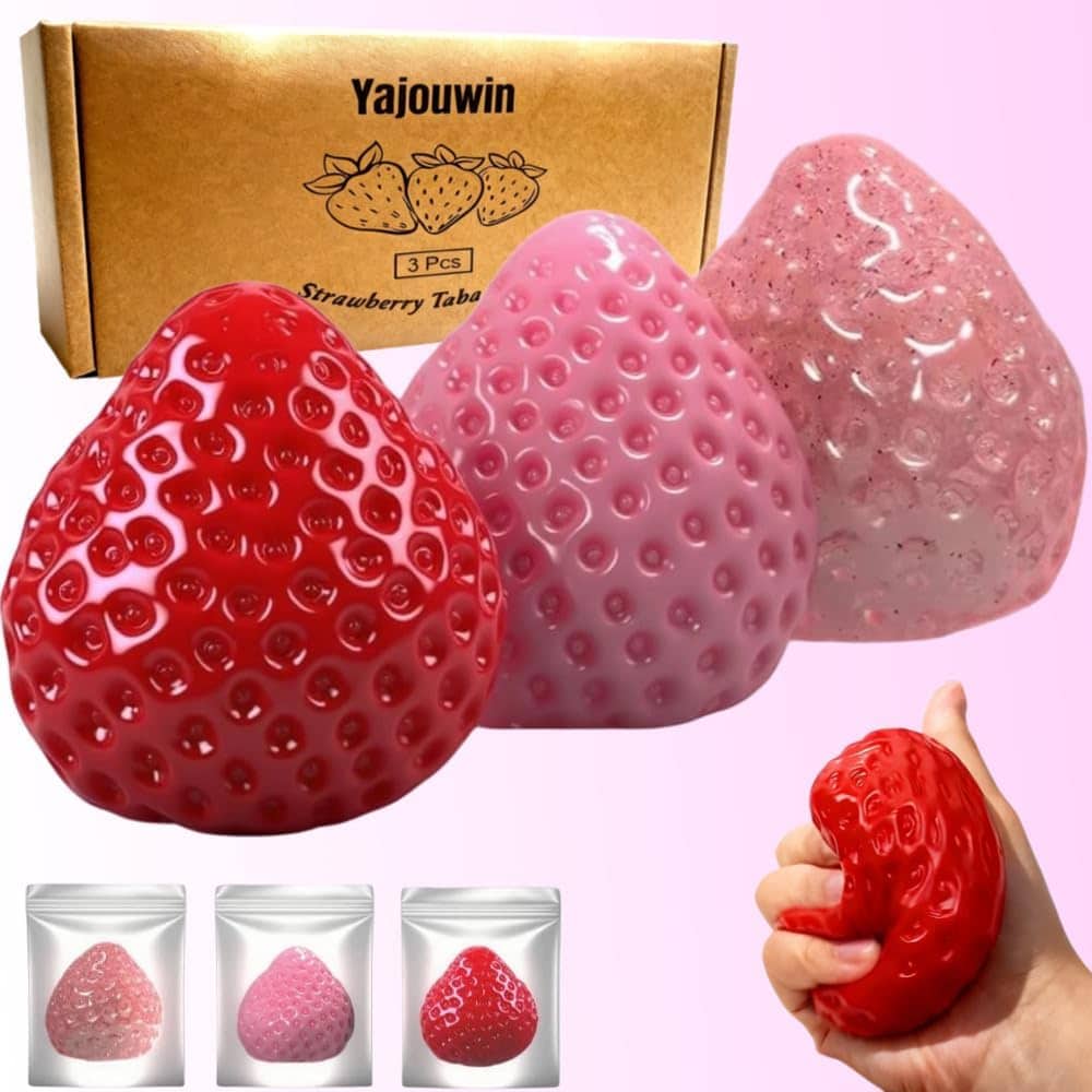 Three strawberry-shaped stress balls in red and pink are shown, with a hand squeezing the red one. A cardboard box and three individual packaging bags are displayed in the background, perfect for Thursday Deals shoppers seeking stress relief.