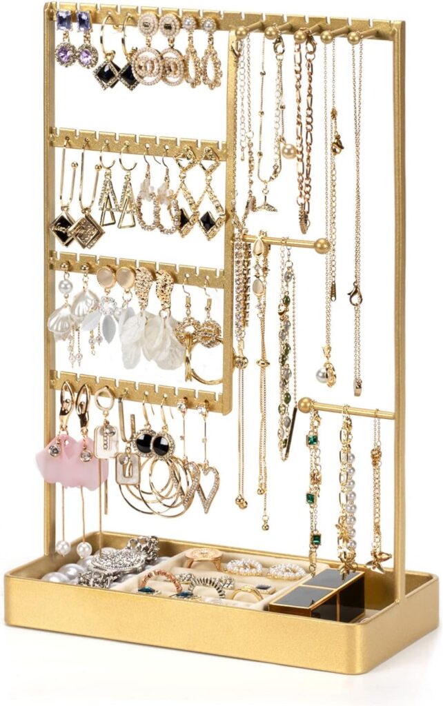 A gold jewelry organizer stand holds a variety of earrings, necklaces, bracelets, and rings, with multiple hanging sections and a tray at the base for additional rings and small accessories.