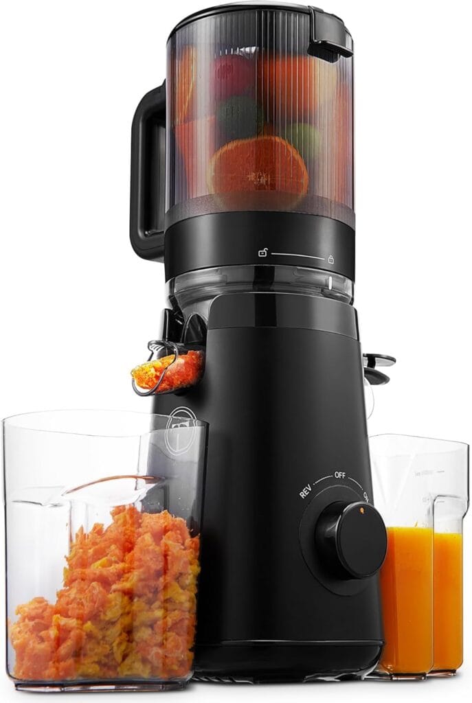 A black juicer machine with fruit inside, dispensing orange juice into a glass on the right and pulp into a container on the left. The juicer has a knob on the front and a handle on the top.