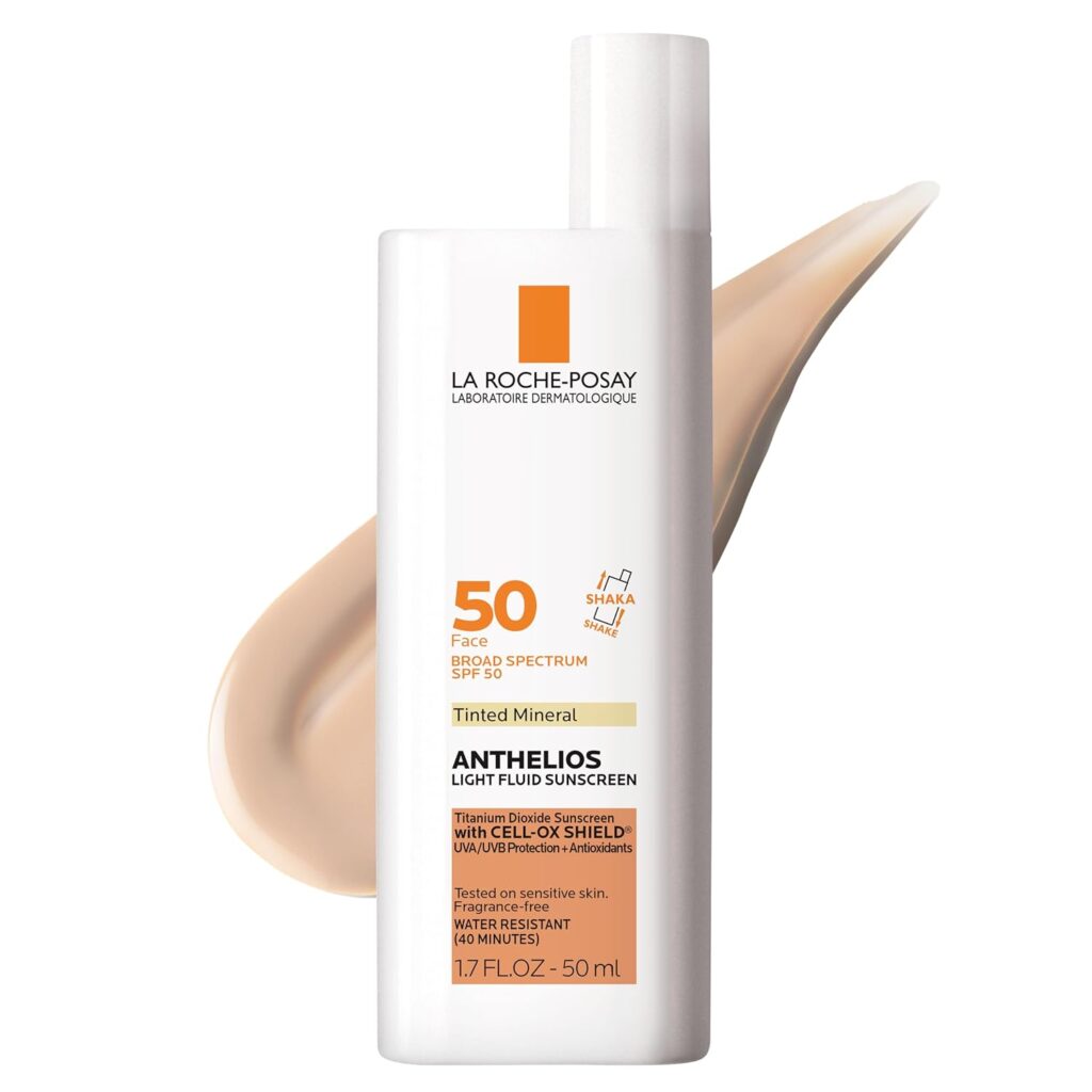A bottle of La Roche-Posay Anthelios Tinted Mineral Light Fluid Sunscreen SPF 50 is shown with a smear of the tinted sunscreen behind it. The label highlights broad spectrum protection and suitability for sensitive skin.