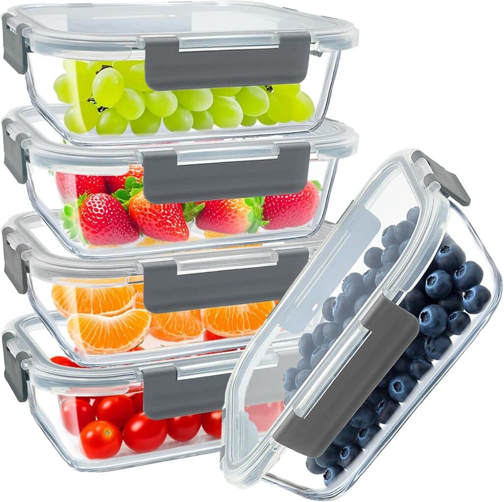 Five clear, rectangular food storage containers with gray lids are stacked, each filled with different fruits: green grapes, strawberries, mandarin orange segments, blueberries, and cherry tomatoes.