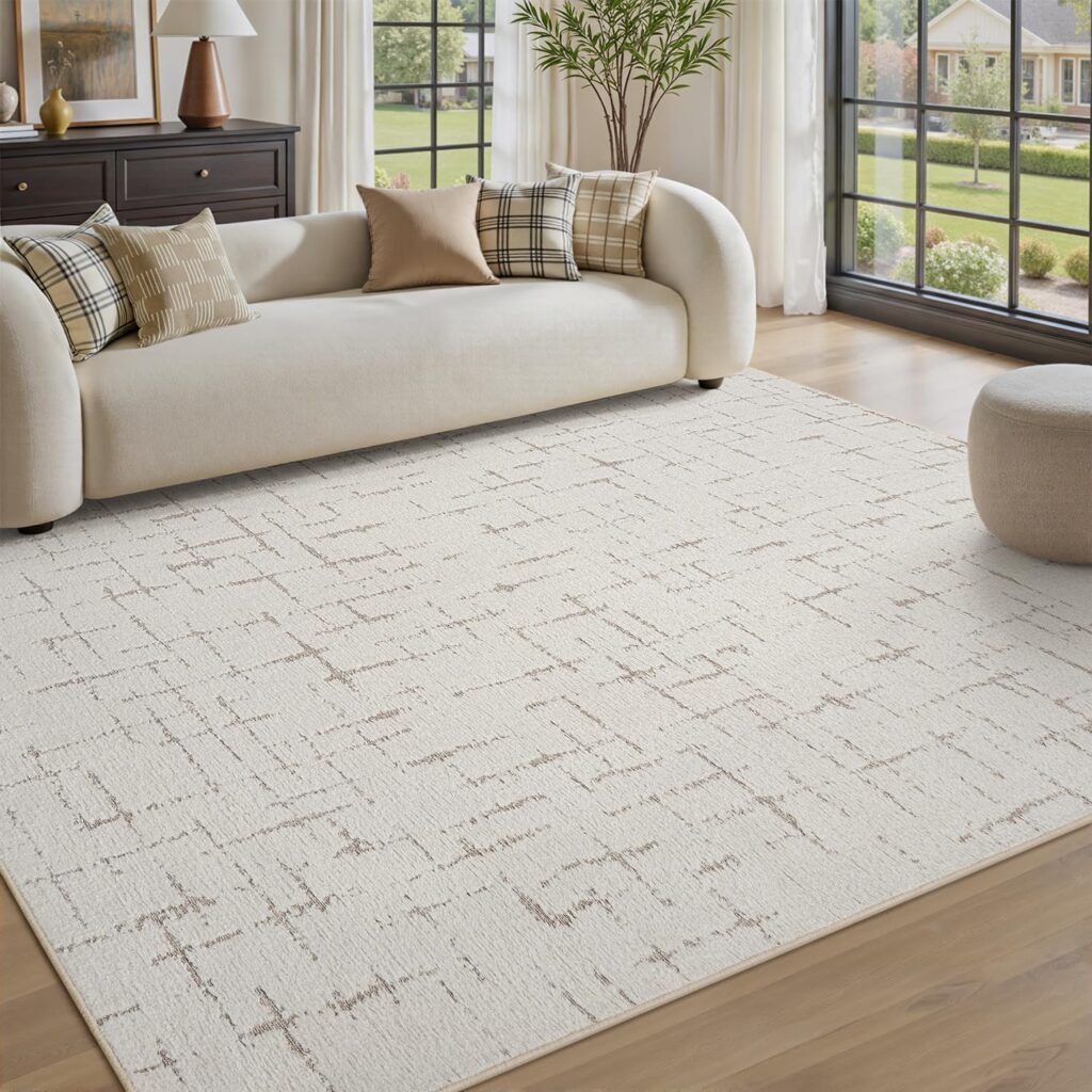 A bright living room with a white patterned rug, a curved cream sofa with plaid and solid pillows, a round ottoman, large windows, and a view of a green yard and neighboring houses.