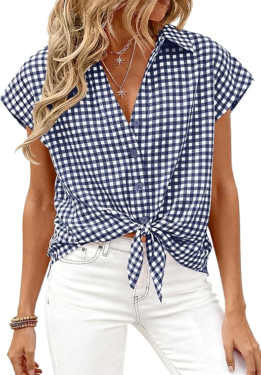 A woman wearing a blue and white gingham short-sleeve button-up shirt tied at the waist, paired with white jeans and layered necklaces. Her wavy blonde hair is loose, and she has bracelets on her wrist.