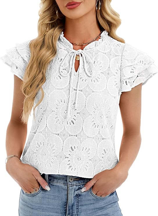 A woman wearing a white lace short-sleeve blouse with a keyhole tie neckline and ruffled sleeves, paired with light blue jeans. She has long wavy blonde hair and accessorizes with necklaces and bracelets.