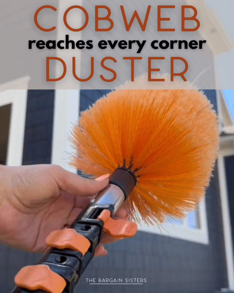 A hand holds an orange cobweb duster with a telescopic handle outside a house. Text above reads, "COBWEB reaches every corner DUSTER.