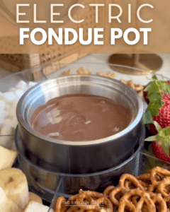 A stainless steel electric fondue pot filled with melted chocolate, surrounded by strawberries, bananas, marshmallows, and pretzels for dipping. The text "Electric Fondue Pot" appears at the top.