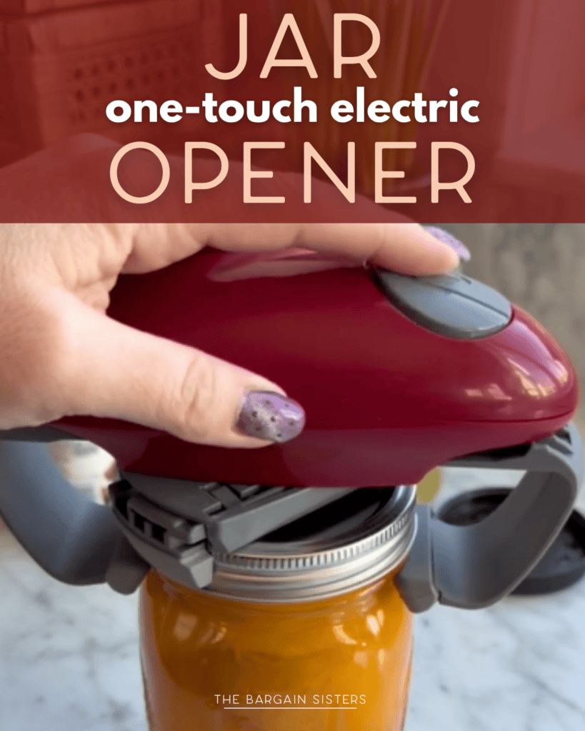 A hand uses a red, one-touch electric jar opener to open a glass jar with orange contents. A marble counter is in the background, and text above reads, "Jar one-touch electric opener.