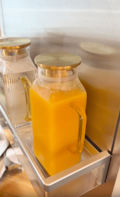 A glass pitcher of orange juice with a gold lid sits in a refrigerator door next to another clear pitcher of water.